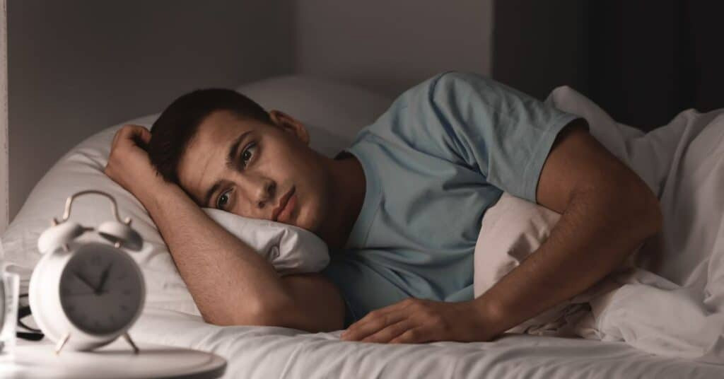 man in bed staring at alarm clock